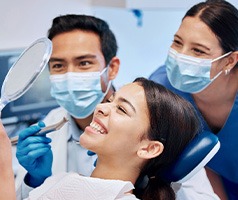 Patient smiling at reflection with dentist and assistant