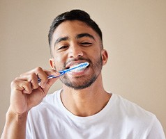 Man smiling while brushing his teeth