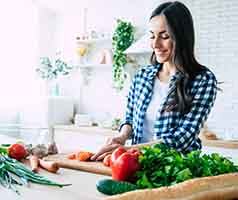 Smiling woman cutting fruits and vegetables in kitchen